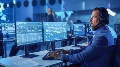 a man wearing headphones and sitting at a desk with multiple monitors