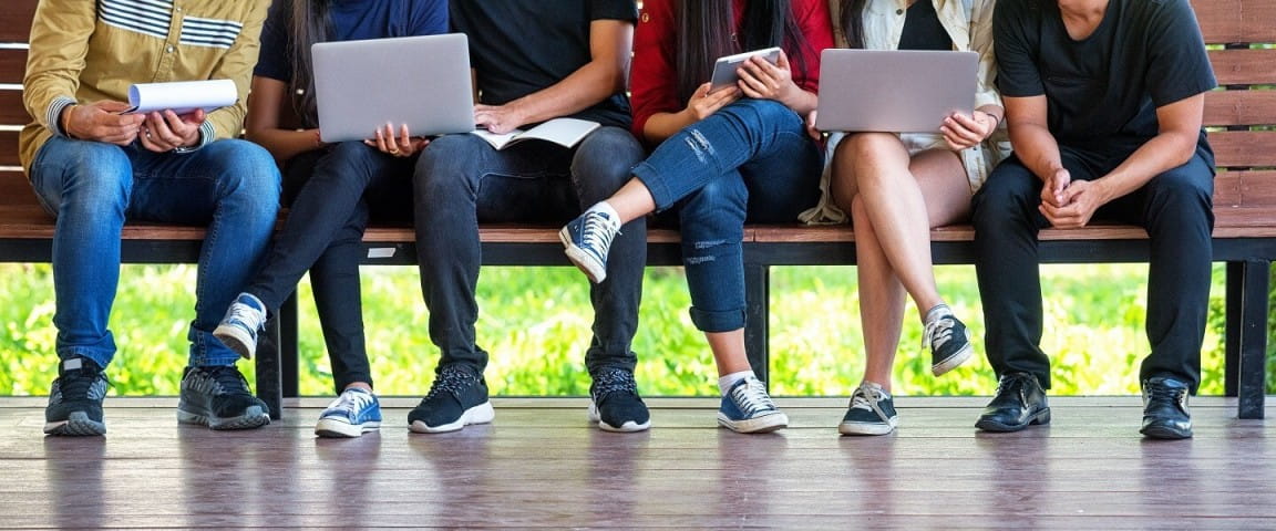 a group of people sitting on a bench with laptops