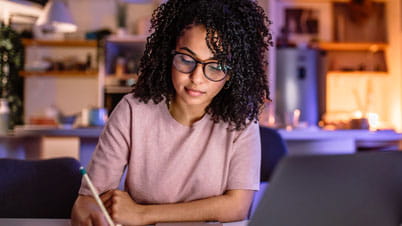 a women writing on a paper in front of a laptop. a women writing on a paper in front of a laptop.